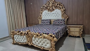 A bedroom with a large bed, ornate headboard, and a nightstand.