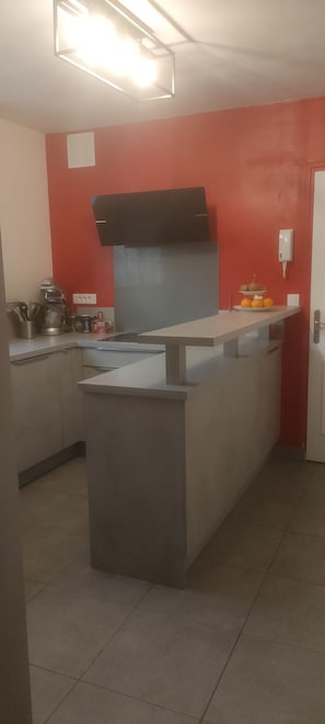 Uma cozinha com ilha central, parede com detalhe em vermelho e coifa preta.