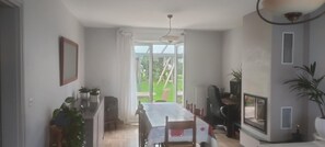 Uma área de refeições com mesa e cadeiras, cozinha com armários e fogão, e uma janela grande com vista para o exterior.