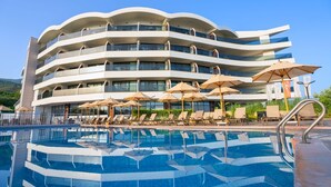 A multi-story hotel with a pool area, sun loungers, and umbrellas. - Seven For Life Thermal Hotel (Kusadasi)