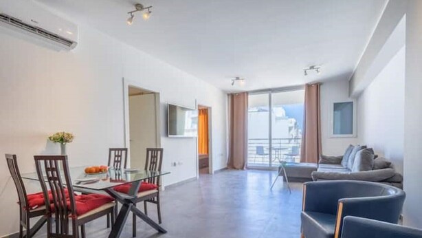 A modern apartment with a dining area, a living room with a sofa, and a balcony with a view.