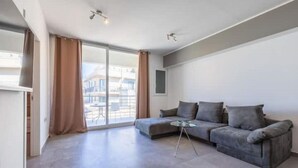 A modern living room with a grey sofa, a glass coffee table, and a sliding glass door leading to an outdoor balcony.