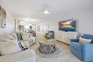 Amplia sala de estar con un conjunto de sofás, una mesa de centro y un televisor sobre un mueble.