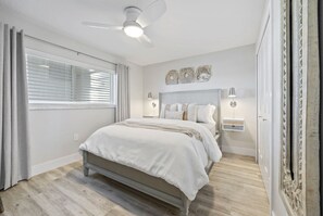 Une chambre à coucher avec un lit, un ventilateur de plafond, des lampes de chevet et une fenêtre avec des stores.