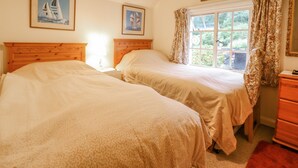 Une chambre avec deux lits, une fenêtre avec des rideaux et des tableaux encadrés accrochés au mur.