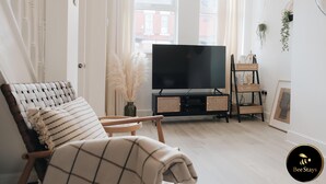 Een moderne woonkamer met een grote flatscreentelevisie, een rieten fauteuil, een bank en een klein bijzettafeltje.