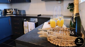 Een aanrecht met een champagnefles, twee glaasjes sinaasappelsap en een geweven onderzetter.