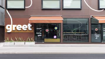A building with a 'greet' sign, large windows, and outdoor seating visible through the glass.