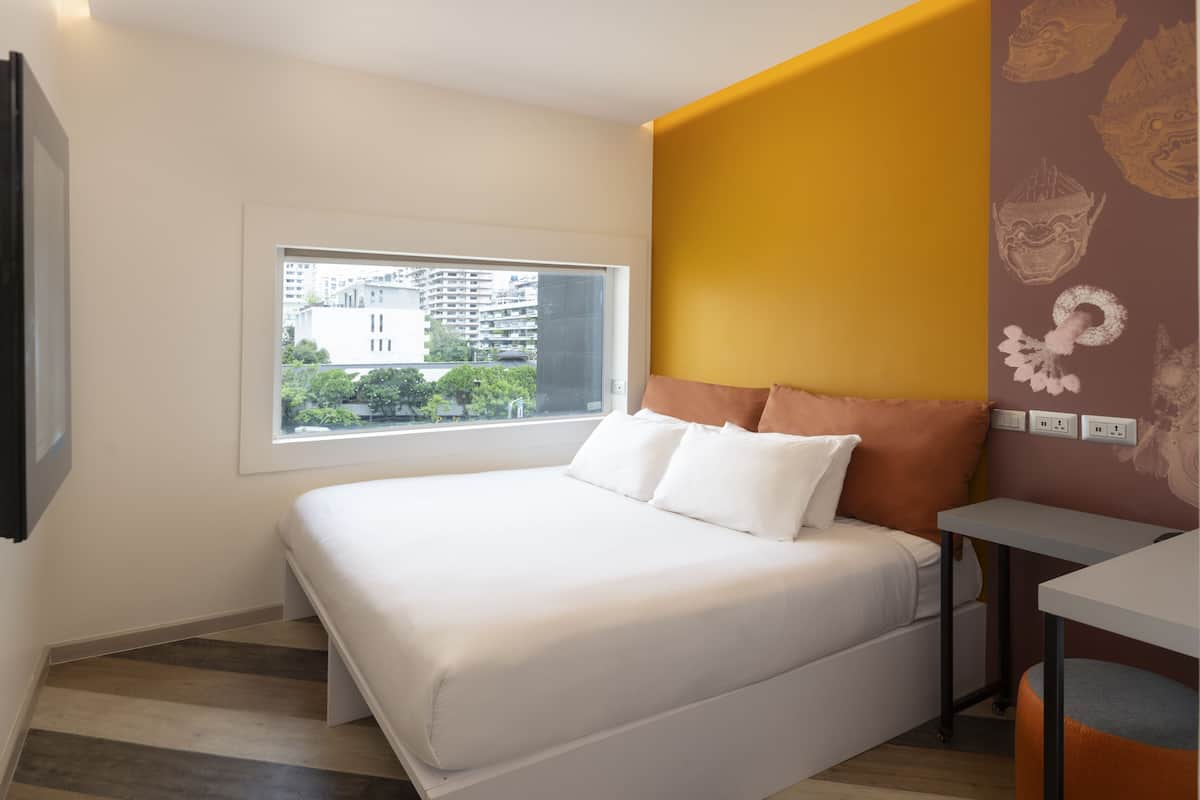Une chambre d’hôtel moderne avec un grand lit, une petite table et une fenêtre donnant sur la ville.