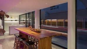 A modern kitchen with a wooden island and bar stools, large windows with a view of a busy street at night. - greet Bangkok Sukhumvit 16 Jono (Bangkok)