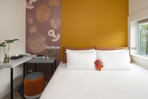 A hotel room with a bed, a desk, a small stool, and a window with a view of greenery. - Jono Bangkok Asok Hotel (Bangkok)