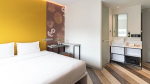Een moderne hotelkamer met een bed, een klein bureau, een badkamer met een wastafel en spiegel, en een decoratieve muur met patronen.