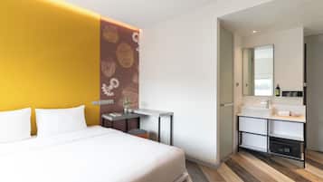 A modern hotel room with a bed, a small desk, a bathroom with a sink and mirror, and a decorative wall with patterns.