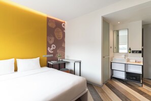 Een moderne hotelkamer met een bed, een klein bureau, een badkamer met een wastafel en spiegel, en een decoratieve muur met patronen.