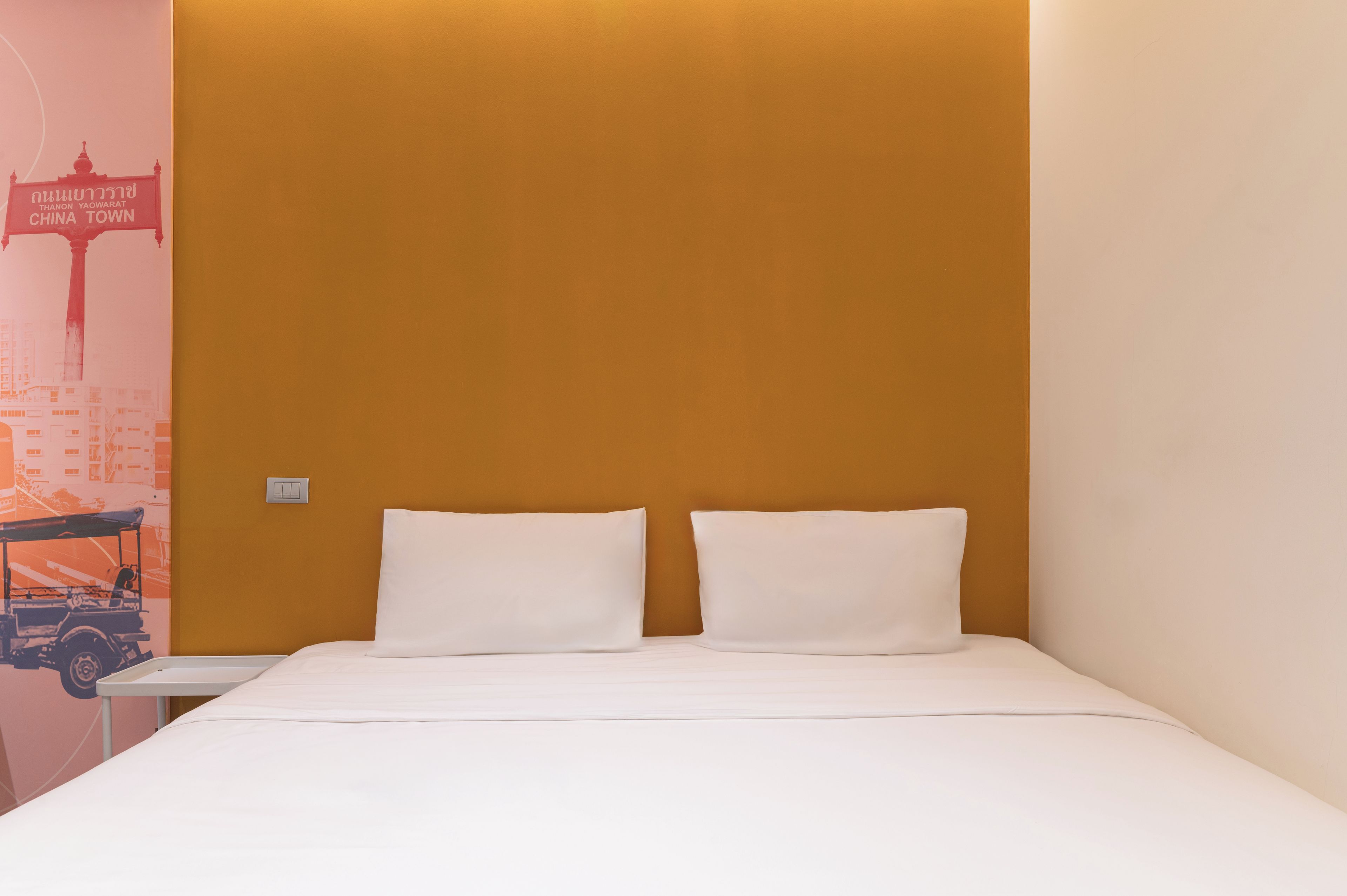 Une chambre d’hôtel avec un lit, deux oreillers, une table de chevet et un mur orné d’une affiche représentant un paysage urbain.