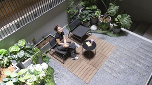 A woman sitting on a bench in a courtyard with potted plants and a small table. - greet Bangkok Sukhumvit 16 Jono (Bangkok)
