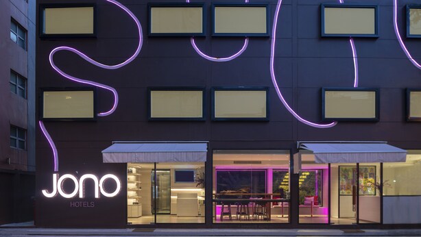 A modern hotel with a neon sign, large windows, and a visible reception area. - greet Bangkok Sukhumvit 16 Jono (Bangkok)