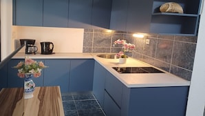 A compact kitchen with dark blue cabinets, a white countertop, a sink, and a decorative vase with flowers. - Apartments Topić (Privlaka)