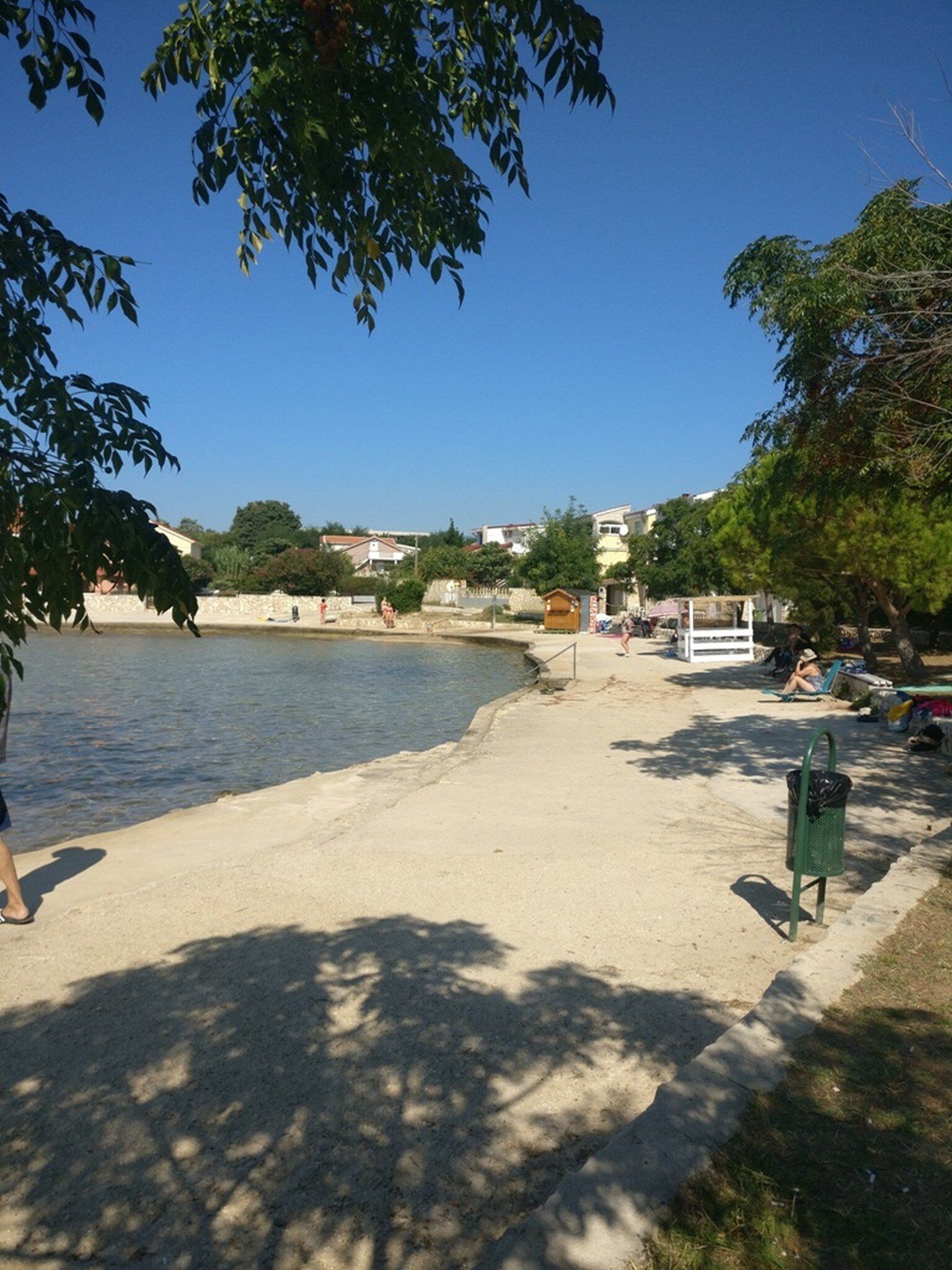 Ein Strand mit sandigem Ufer, einer kleinen Holzkonstruktion und einigen Personen.