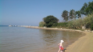 A beach with a clear view of the water, a sandy shore, and a child playing with a toy. - Apartments Topić (Privlaka)