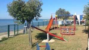 A playground with a seesaw, a slide, and swings, located near a body of water. - Apartments Topić (Privlaka)