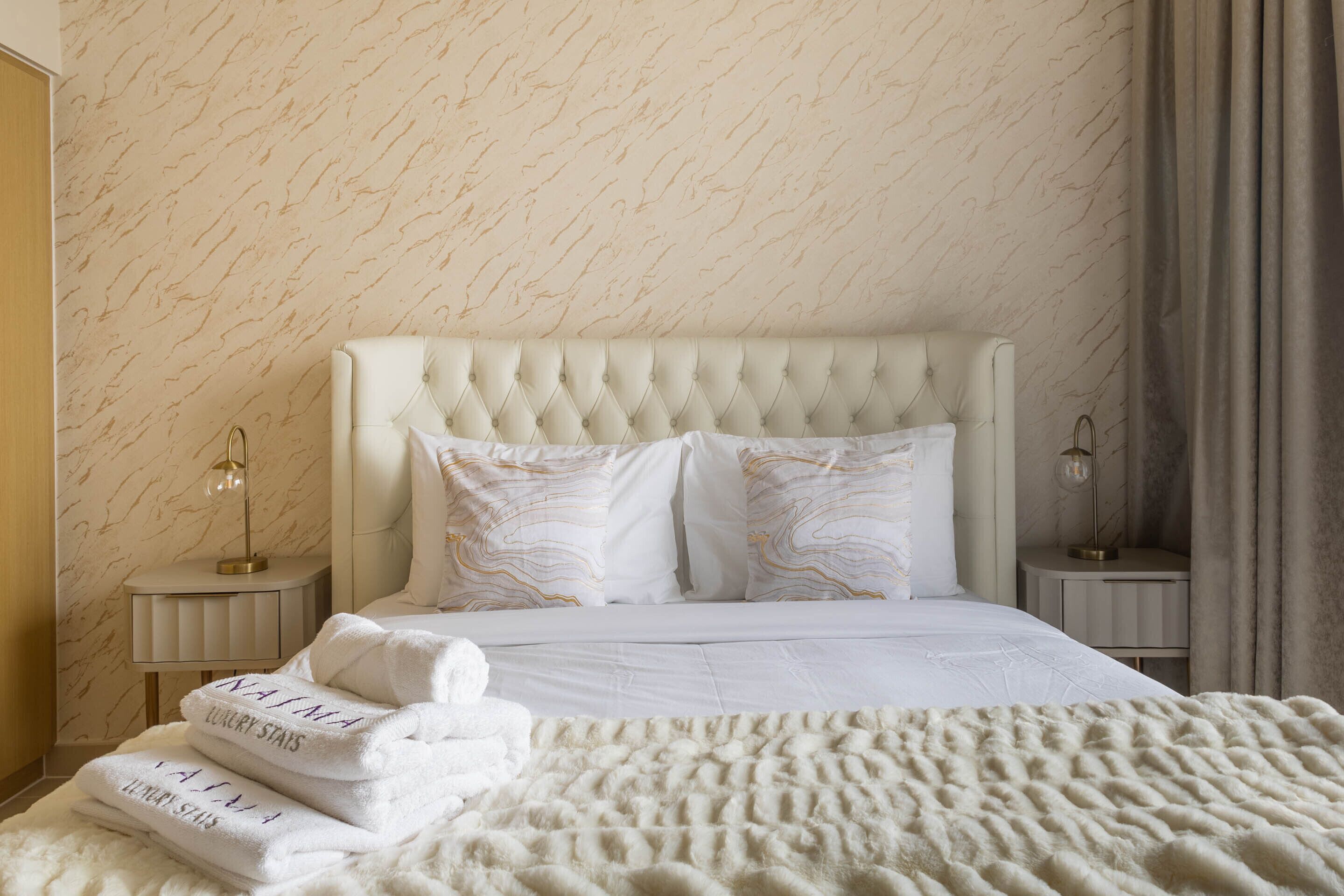 A neatly made bed with a tufted headboard, white bedding, and two bedside lamps.