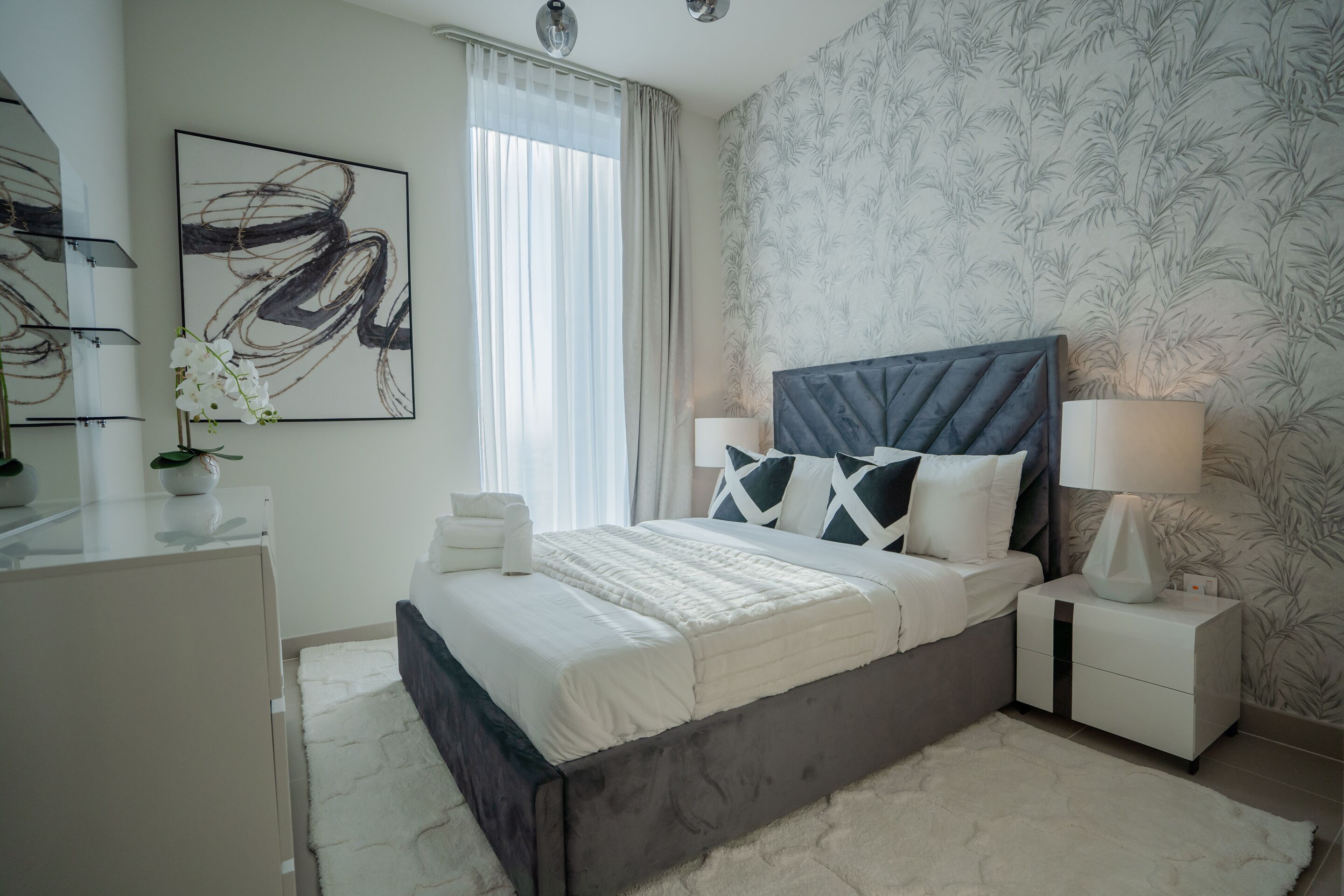 Een moderne slaapkamer met een groot bed, nachtkastjes, een spiegel en een raam met gordijnen.