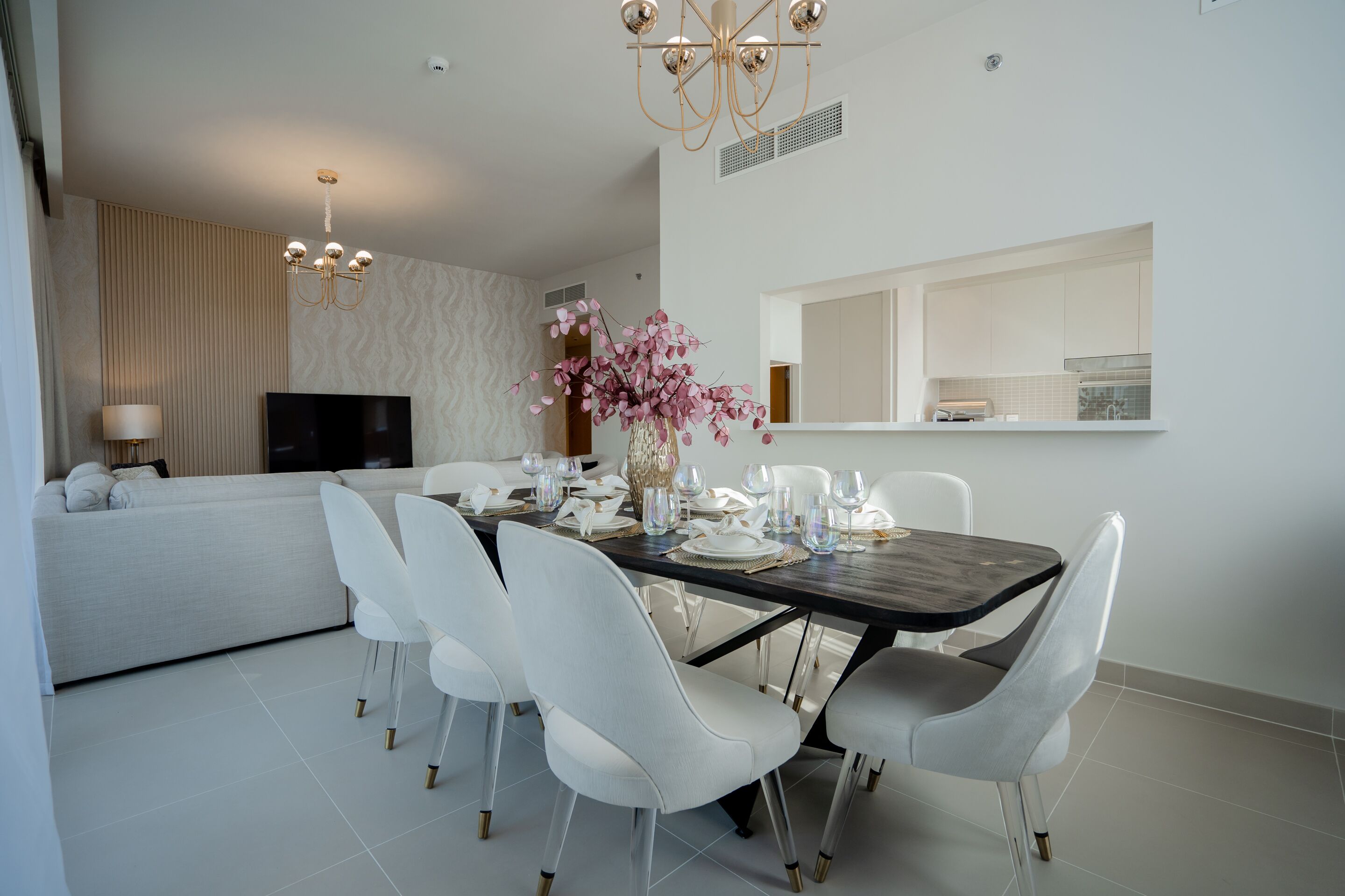 A modern dining area with a dark wooden table, white chairs, and a decorative vase with pink flowers.