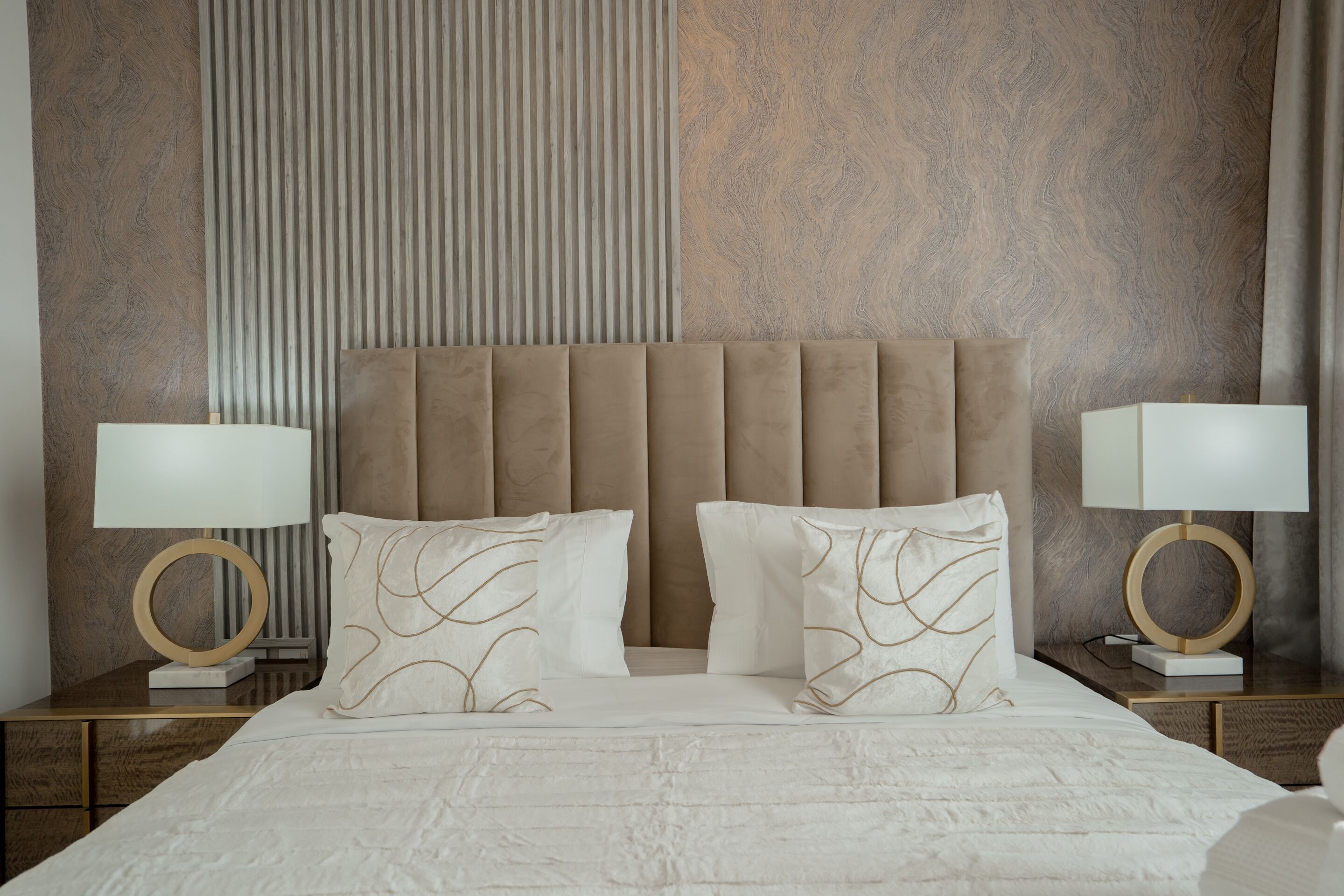 A neatly made bed with a tufted headboard, two bedside tables with lamps, and a textured wall behind.