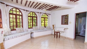 A room with a built-in bench along the wall, large arched windows, a ceiling fan, and a small table with a chair. - Villa Pundamilia, Private Pool, Free Wifi, Secure (Diani Beach)