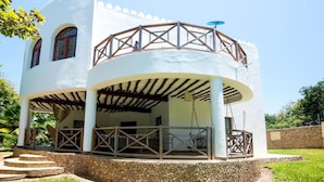 A white building with a covered patio, a balcony, and a stone wall surrounding the property. - Villa Pundamilia, Private Pool, Free Wifi, Secure (Diani Beach)