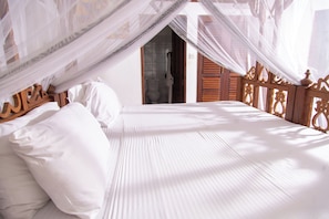 A bed with white linens and a wooden headboard, a wooden door, and a white wall. - Villa Pundamilia, Private Pool, Free Wifi, Secure (Diani Beach)
