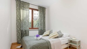 Une chambre à coucher avec un lit, une table de chevet, une fenêtre avec des rideaux et un radiateur.