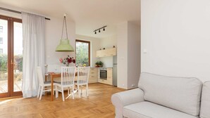 Un salon moderne comprenant un canapé, une table à manger avec des chaises et un coin cuisine avec des placards et un luminaire suspendu.