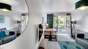 A modern living room with a sofa, a dining table, and chairs. There is a view of the outdoors through large windows. - Week2Week Gosforth apartment w balcony (Newcastle-upon-Tyne)