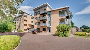 A multi-story residential building with balconies, a parking area, and a well-maintained lawn. - Week2Week Gosforth apartment w balcony (Newcastle-upon-Tyne)