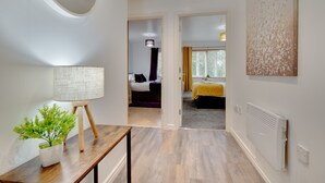 A modern hotel room with a wooden floor, a bed with a yellow bedspread, a large abstract painting on the wall, and a potted plant on a wooden table. - Week2Week Gosforth apartment w balcony (Newcastle-upon-Tyne)
