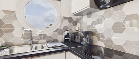 Una cocina compacta con un ventanal redondo, estufa integrada y cafetera.