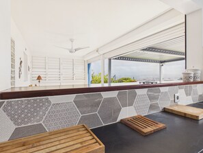 A modern kitchen with a view of the sea, a ceiling fan, and a tiled backsplash.