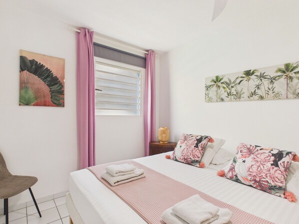 A bedroom with a bed, pillows, a chair, a window with curtains, and wall art.