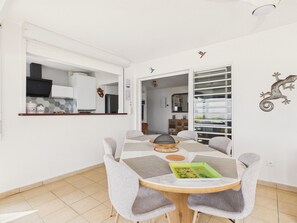 A dining area with a round table, grey upholstered chairs, and a view into the kitchen.