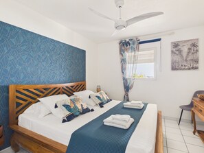 A bedroom with a wooden bed, a ceiling fan, a window with curtains, and a wall painting.