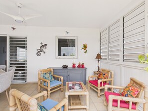 A room with wicker furniture, a ceiling fan, decorative wall art, and a window with blinds.