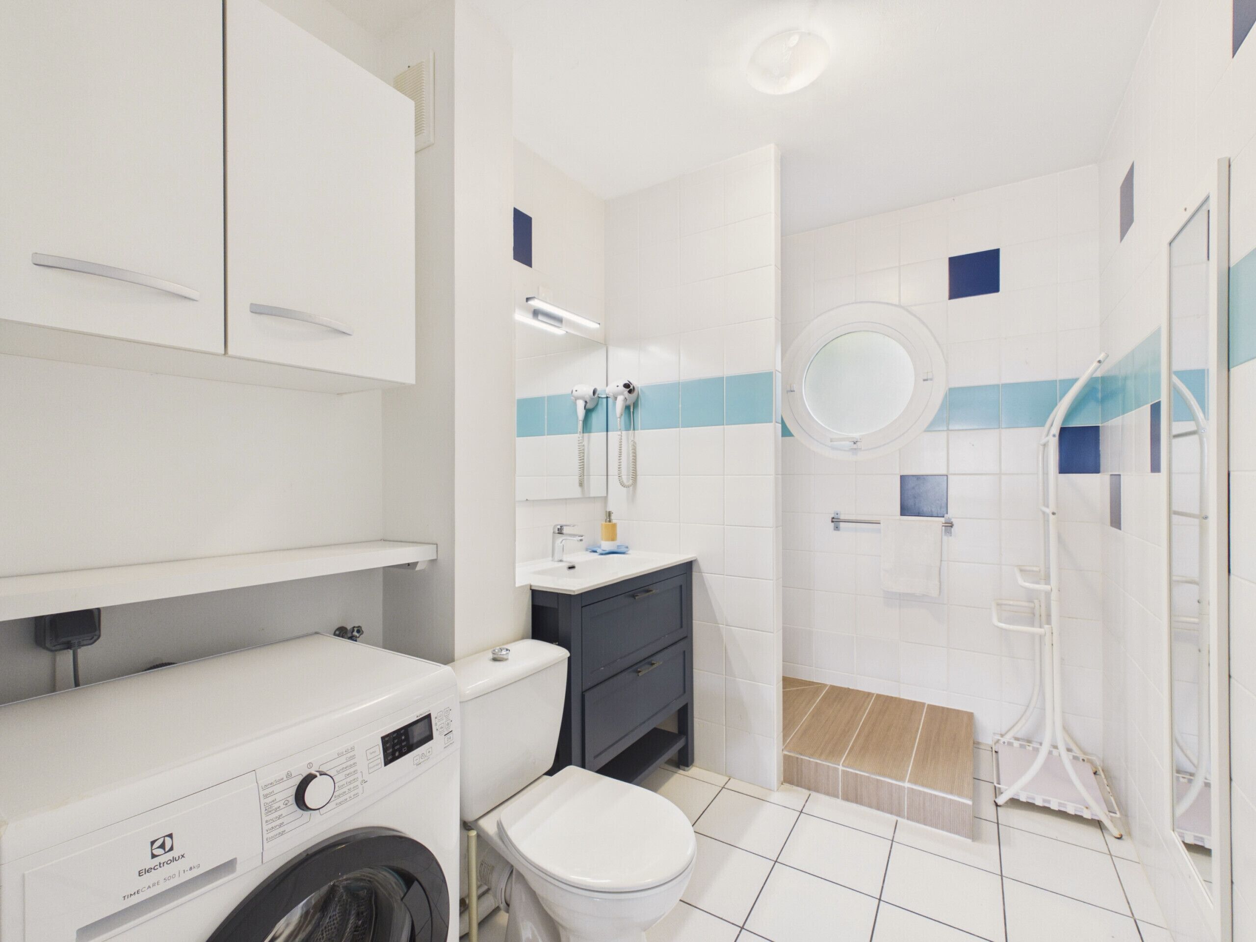 A modern bathroom with a washing machine, toilet, sink, and shower.