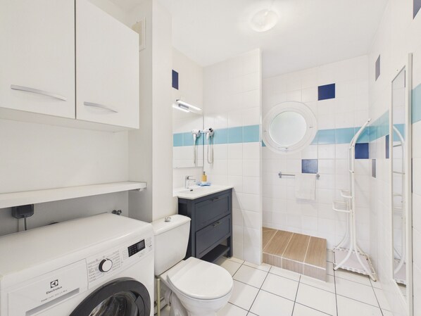 A modern bathroom with a washing machine, toilet, sink, and shower.