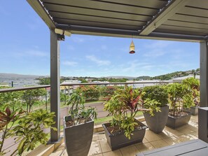A balcony with potted plants, a view of the sea, and a clear sky.