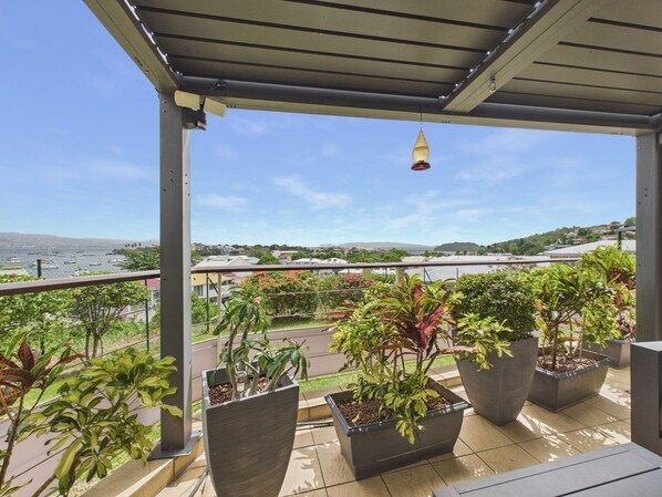 A balcony with potted plants, a view of the sea, and a clear sky.