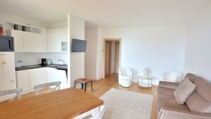 A modern apartment with a wooden dining table, white chairs, a beige sofa, and a small white armchair. - Apartment Borgo Montagna With Pool (San Zeno di Montagna)