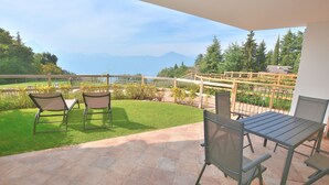 A patio with two chairs and a table, a grassy lawn, and a view of mountains. - Apartment Borgo Montagna With Pool (San Zeno di Montagna)