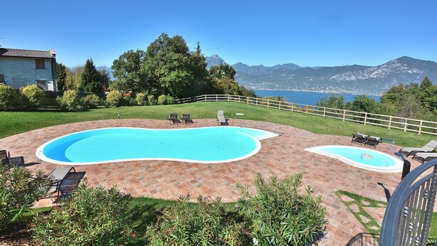 A backyard with a swimming pool, lounge chairs, and a view of mountains and a lake. - Apartment Borgo Montagna With Pool (San Zeno di Montagna)